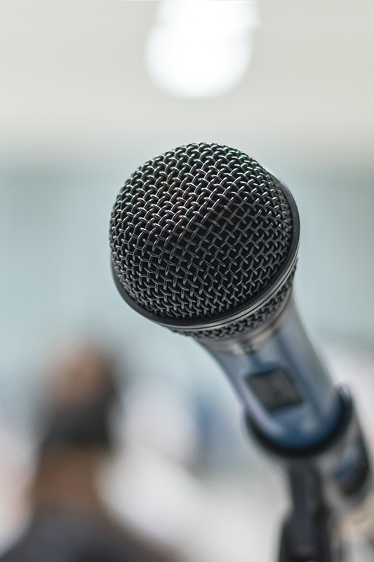 Close up of black microphone in front of blurred audience.